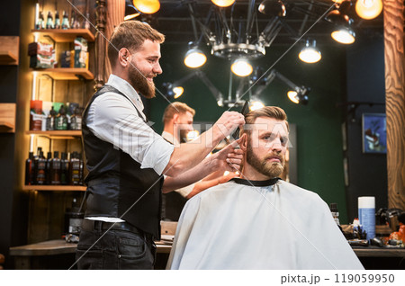 Hairdresser making final touches in new haircut. Comfortable atmosphere in modern barbershop. Stylish barber using professional comb to style hair. Hairdresser making final touches in new haircut. Comfortable atmosphere in modern barbershop. Stylish barber using professional comb to style hair. 119059950