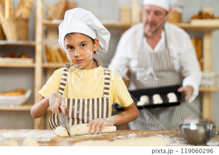 Little girl, baker assistant, cutting raw dough with knife Little girl, baker assistant, cutting raw dough with knife 119060296