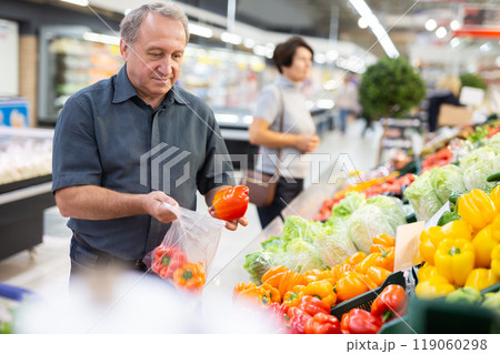 Mature customer selects bell peppers with interest in grocery department of supermarket 119060298