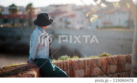 Tourist woman wearing black hat posing at the walls of Castle in Antibes, France Tourist woman wearing black hat posing at the walls of Castle in Antibes, France 119060478