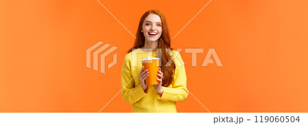 Cheerful cute redhead curly girlfriend holding popcorn chat with boyfriend before movie start at cinema, smiling joyfully, like attend premieres in theatres, standing overjoy orange background 119060504
