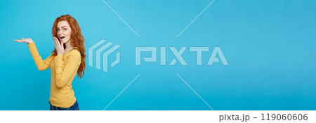Fun and People Concept - Headshot Portrait of happy ginger red hair girl with presenting hand away and shocking expression. Pastel blue background. Copy Space. Fun and People Concept - Headshot Portrait of happy ginger red hair girl with presenting hand away and shocking expression. Pastel blue background. Copy Space. 119060606