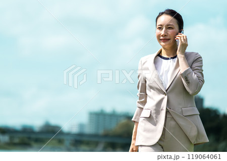 屋外を歩きながらスマホで会話するスーツ姿の女性 119064061