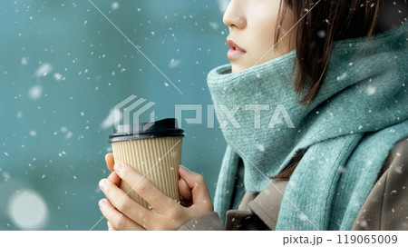 雪の降る冬の街角で暖かい飲み物を飲む女性 119065009