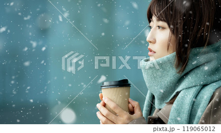 雪の降る冬の街角で暖かい飲み物を飲む女性 119065012