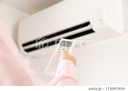 エアコンのリモコンを持つ女性の手元 119065404