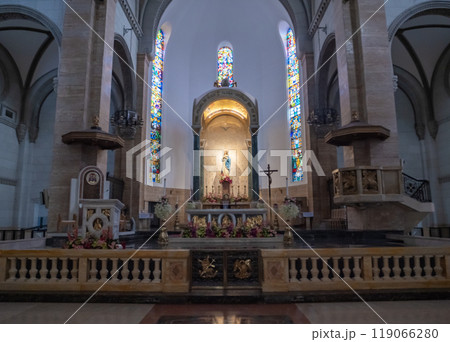 The interior of a church showcases stained glass windows casting colorful light on the altar. Floral arrangements enhance the sacred atmosphere. The interior of a church showcases stained glass windows casting colorful light on the altar. Floral arrangements enhance the sacred atmosphere. 119066280