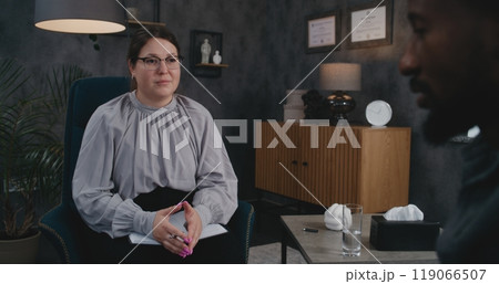 Female therapist sits in chair, talks to African American adult man, provides therapy Female therapist sits in chair, talks to African American adult man, provides therapy 119066507