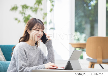 パソコンを操作しながら電話をする女性 119067548