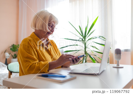 Elderly woman working on laptop computer, smiling, working from home. Trendy woman working on laptop from home 119067792