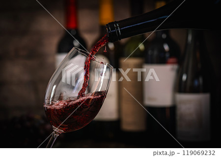 Pouring Red Wine into Glass with Bottles and Grapes 119069232