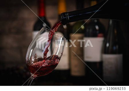 Pouring Red Wine into Glass with Bottles and Grapes 119069233