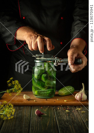 Manual seaming key in the hands of a cook for preserving cucumbers in a glass jar. Pickled cucumber for long-term storage 119070941