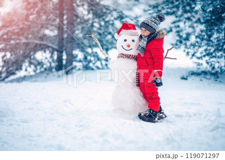 Boy in warm clothing bonding snowman in natural park. Boy in warm clothing bonding snowman in natural park. 119071297