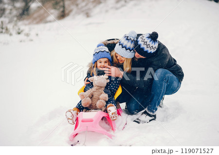 Family have fun in a winter park. Stylish mother in a blue jacket. Little girl on a pink sled. Father with cute daughter 119071527
