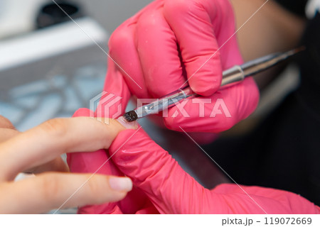 Professional nail technician applying base coat and gel polish using a brush during a manicure session. Professional nail technician applying base coat and gel polish using a brush during a manicure session. 119072669