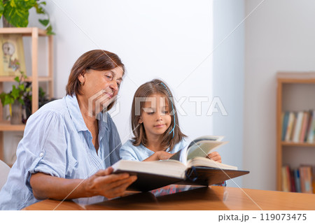 Girl going through book with grandmother on table Girl going through book with grandmother on table 119073475