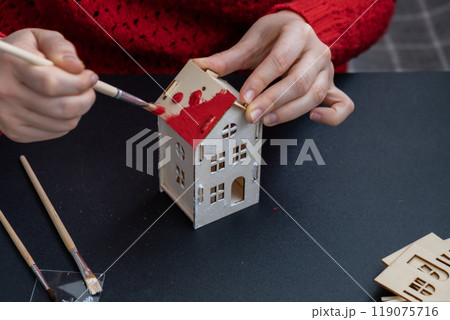 Process of preparing for Christmas and New Year eve. Unrecognizable woman in red sweater painting 3D craft wooden houses DIY. Responsible ecological zero waste handmade decoration. Children hobby Process of preparing for Christmas and New Year eve. Unrecognizable woman in red sweater painting 3D craft wooden houses DIY. Responsible ecological zero waste handmade decoration. Children hobby 119075716