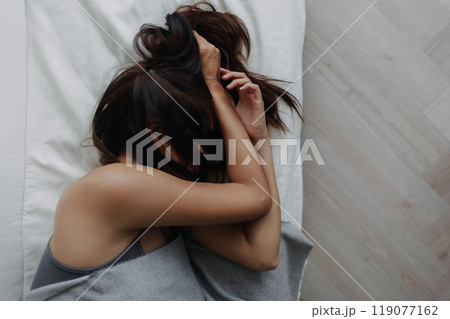 Woman does not want to wake up, using her arms to block the light. 119077162