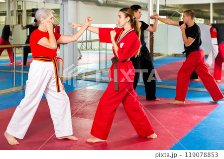 Elderly woman sparring with girl during martial arts training 119078853
