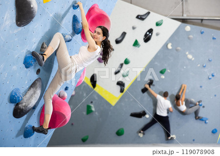Motivated young girl climbing without ropes and harnesses on artificial bouldering wall in fitness center 119078908