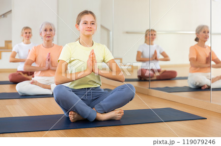 Teen girl with family in lotus position practices yoga in gym 119079246