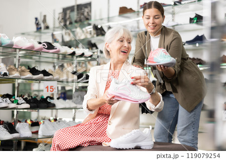 Elderly mom sits on bench and asks her daughter to advise fashionable sneakers for fitting 119079254