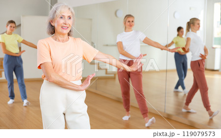 Positive woman doing aerobics exercises with group of people in dance center Positive woman doing aerobics exercises with group of people in dance center 119079573