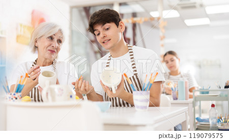 Cheerful guy working with elderly mother in family pottery studio Cheerful guy working with elderly mother in family pottery studio 119079575
