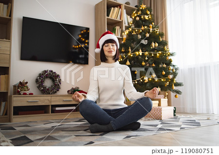 Young woman meditating by Christmas tree in cozy home setting Young woman meditating by Christmas tree in cozy home setting 119080751