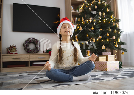 Young girl meditating by Christmas tree with Santa hat Young girl meditating by Christmas tree with Santa hat 119080763