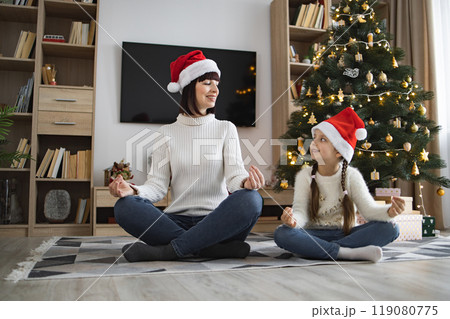 Mother and daughter celebrating Christmas with yoga by tree Mother and daughter celebrating Christmas with yoga by tree 119080775