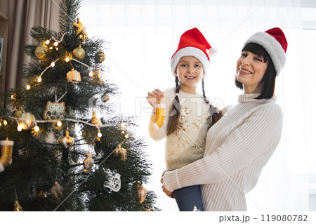 Mother and daughter celebrating Christmas by decorated tree 119080782