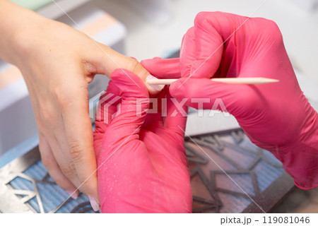 Close up manicure master uses an orange stick to remove cuticula pro clients fingers.  119081046