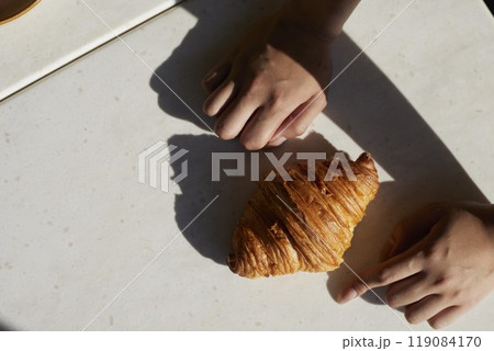 Hands and one croissant on white table with hard light Hands and one croissant on white table with hard light 119084170