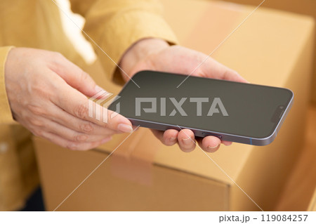 スマホを持つミドル女性とダンボールに入った引っ越しの荷物 スマホを持つミドル女性とダンボールに入った引っ越しの荷物 119084257