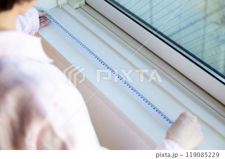 マンションの窓辺でカーテンのサイズを測るミドル女性 119085229