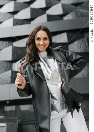Smiling woman in a black leather jacket and silver shirt poses for the camera 119085644