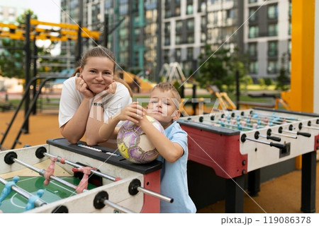 A joyful moment shared between a mother and son at a city playground, enjoying foosball and soccer 119086378