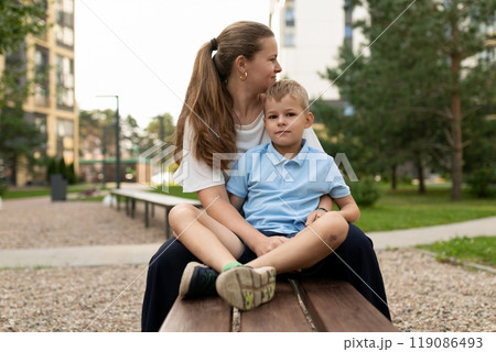 A mother and her son sharing a warm moment together while sitting on a bench in the park during the 119086493