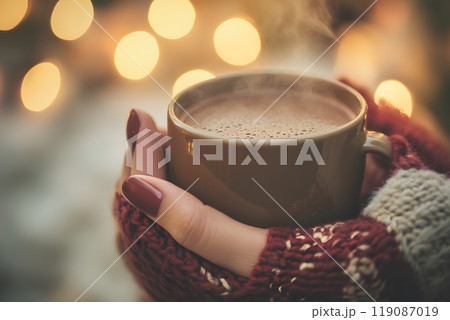 Cozy hands holding a steaming mug of hot chocolate with festive ambiance. Winter warmth concept 119087019