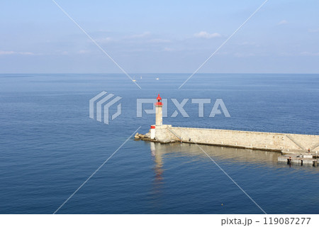 A calm seaside scene with a red lighthouse standing on the edge of a pier in Corsica, France A calm seaside scene with a red lighthouse standing on the edge of a pier in Corsica, France 119087277