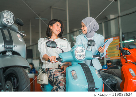 young woman chats with a veiled saleswoman on a new motorcycle young woman chats with a veiled saleswoman on a new motorcycle 119088624