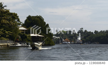 Beautiful river walk with tropical village. Action. River boats floating among jungles and settlements. River with village and Buddha statue in jungle on sunny summer day Beautiful river walk with tropical village. Action. River boats floating among jungles and settlements. River with village and Buddha statue in jungle on sunny summer day 119088640