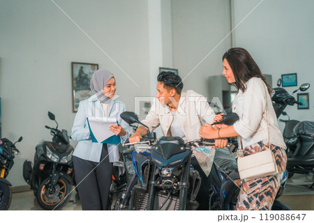 male and female couple trying out a new motorcycle with saleswoman chatting male and female couple trying out a new motorcycle with saleswoman chatting 119088647