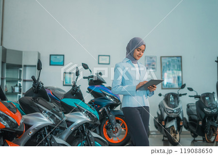 Muslim woman using a tablet with a background of a motorcycle showroom 119088650