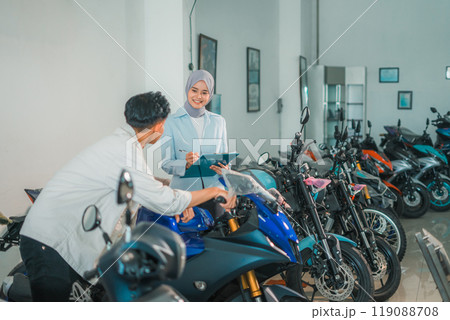 saleswoman wearing a hijab with a male customer looking at a motorcycle saleswoman wearing a hijab with a male customer looking at a motorcycle 119088708