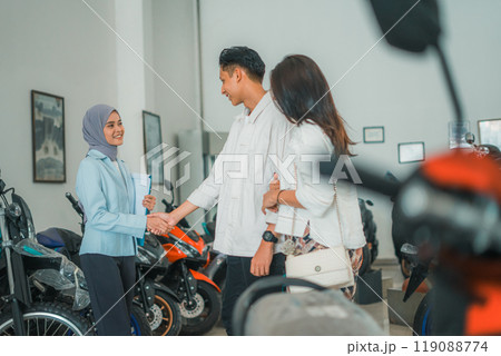 a veiled saleswoman shaking hands with a buyer at a vehicle showroom 119088774