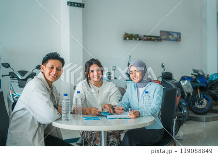 young Asian couple and saleswoman smile while sitting in a motorcycle showroom 119088849