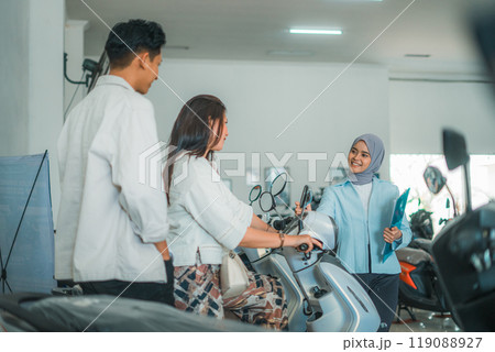 Asian woman and man trying out a new motorcycle served by a saleswoman Asian woman and man trying out a new motorcycle served by a saleswoman 119088927